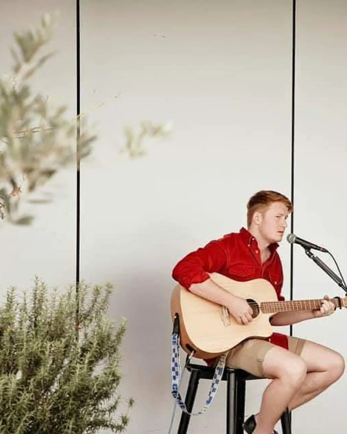 Red playing acoustic guitar outdoors in a red shirt
